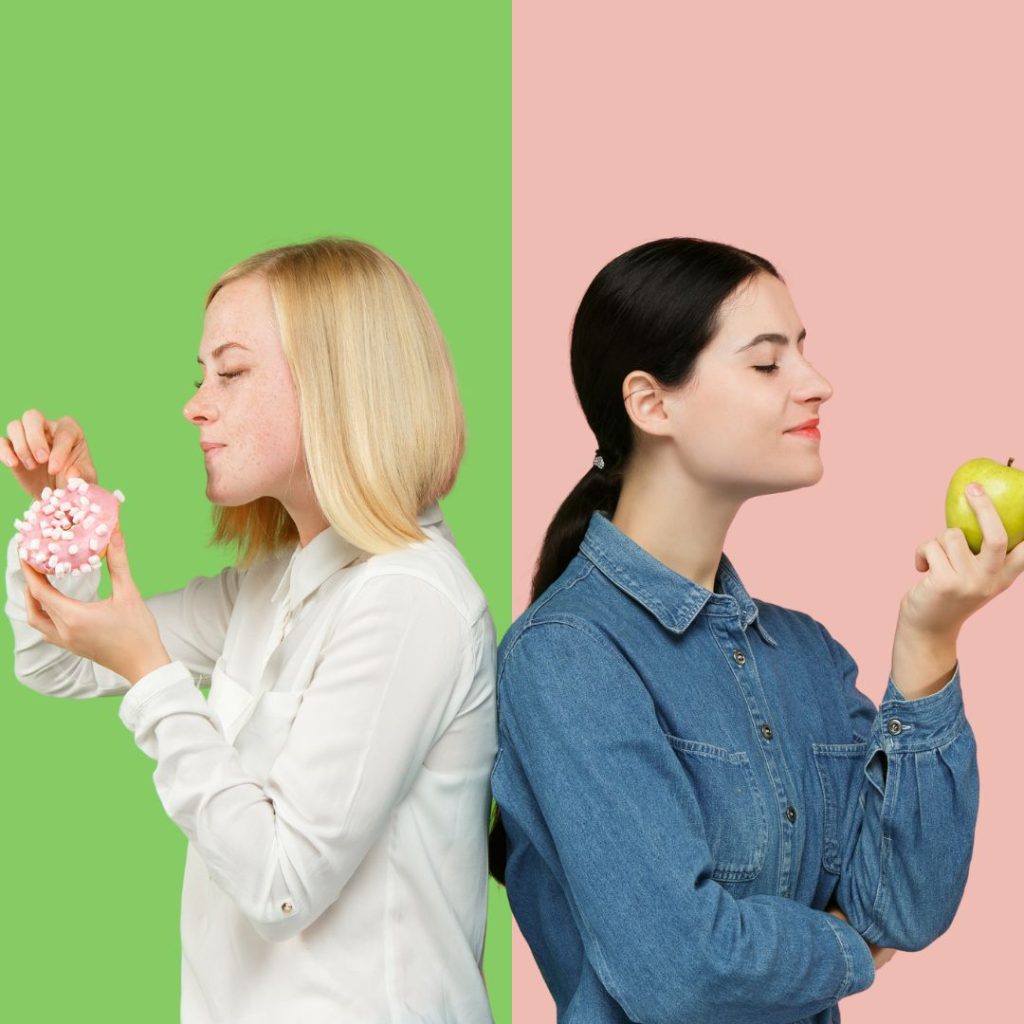 Two women holding different foods. One holding an apple, the other holding a donut.